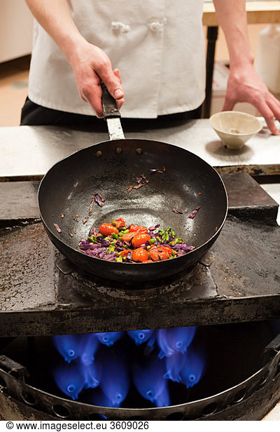 Male chef frying with wok in commercial kitchen