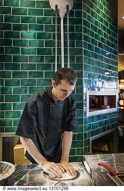 Male chef preparing pizza dough in commercial kitchen