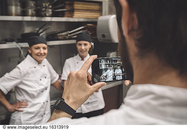 Male chef taking photograph of female coworkers in commercial kitchen