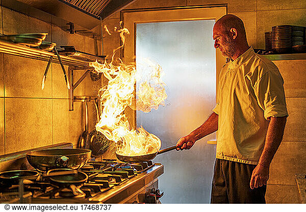 Male chef with flaming pan cooking in kitchen