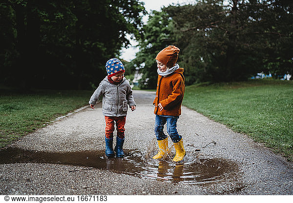 Male children jumping in the puddles at the park on rainy day