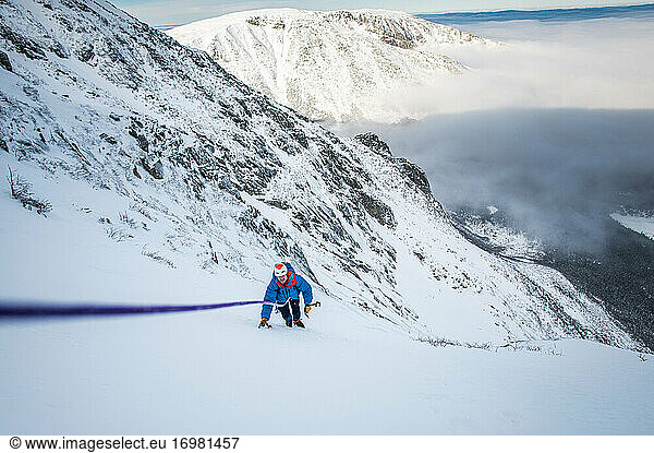 Male climber being belayed up steep snow with cloud inversion behind