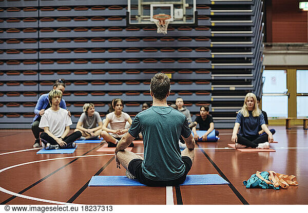 Male coach teaching exercise to students in sports court