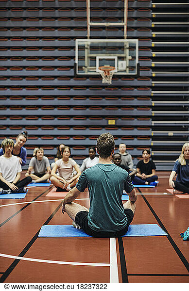 Male coach teaching yoga to male and female students in sports court