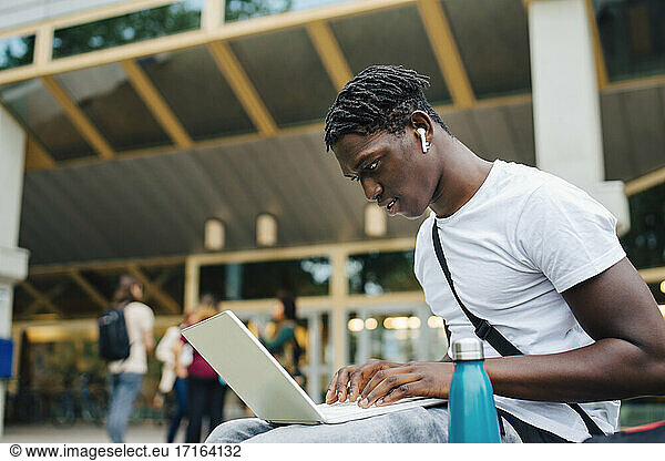 Male college student studying online on laptop in university campus