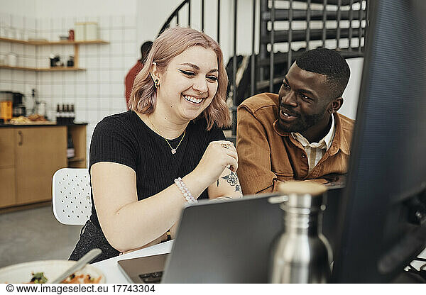Male computer programmer discussing while looking at happy female colleague in tech start-up office