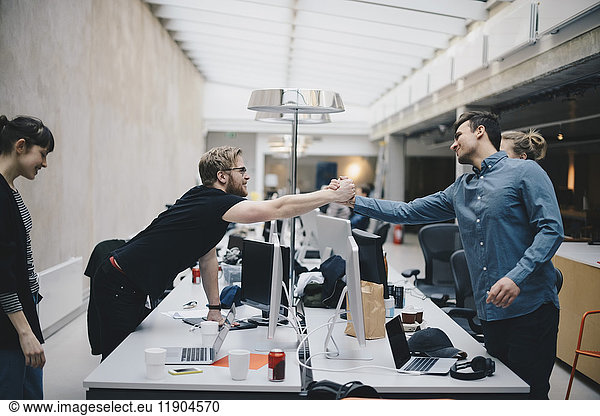 Male computer programmers holding hands over desk in office