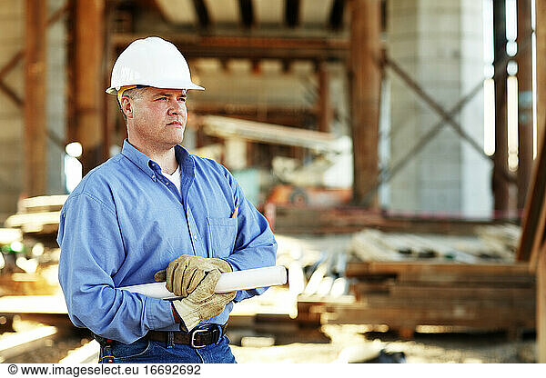 Male construction foreman holding plans looking off camera