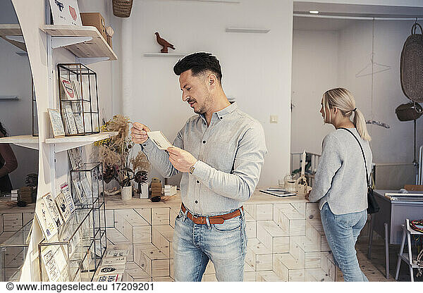Male customer looking at greeting card while standing by woman in design studio