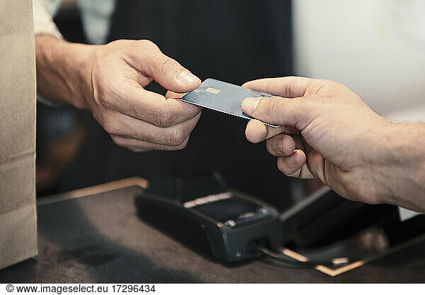 Male customer making payment through credit card at organic shop