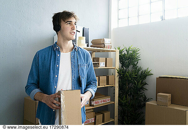 Male customer service representative with box talking through headphones in warehouse