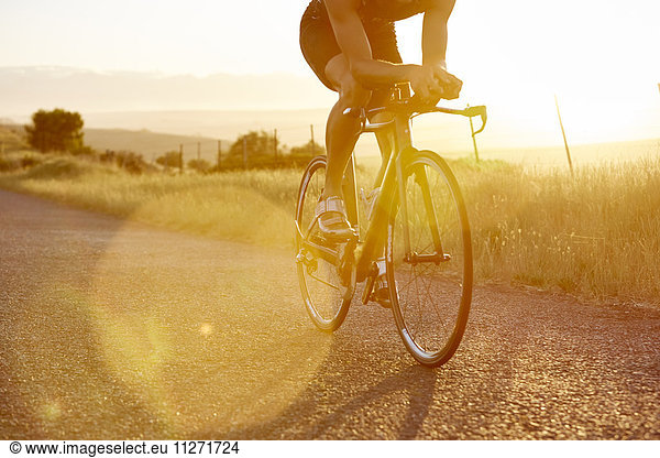 Male cyclist riding bike on sunny sunrise rural road