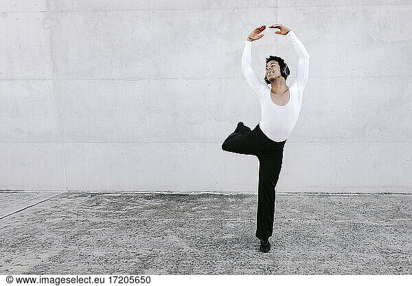 Male dancer balancing on one leg while dancing in white wall