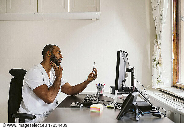 Male doctor consulting on video call through smart phone while sitting at desk