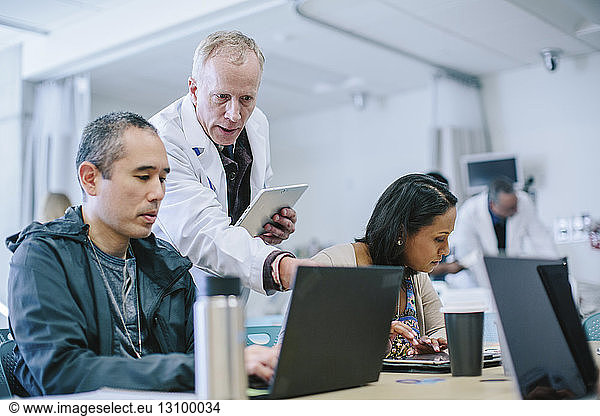 Male doctor discussing with coworkers over laptop computer in medical room