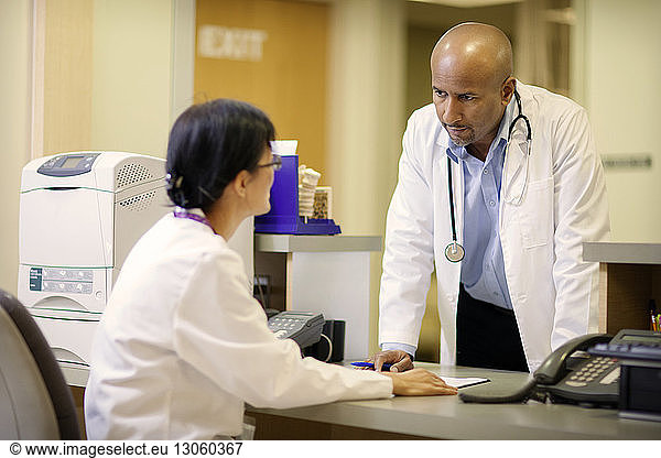 Male doctor discussing with female doctor at desk in hospital