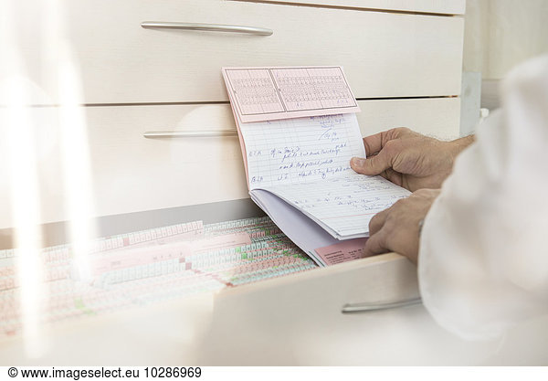 Male doctor reading the index card of a patient by drawers  Munich  Bavaria  Germany