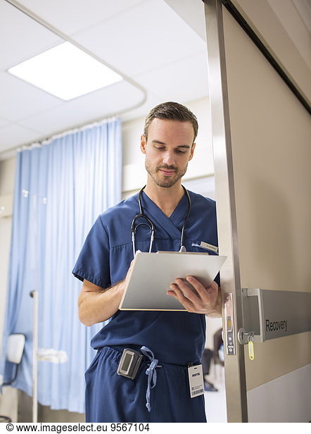 Male doctor standing in doorway  taking notes on clip board in hospital