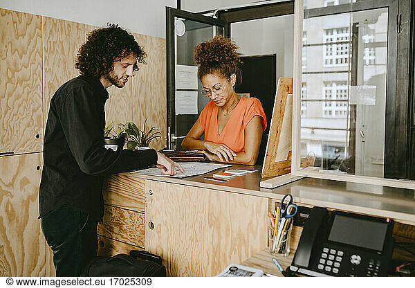 Male entrepreneur discussing with female colleague over document at coworking office
