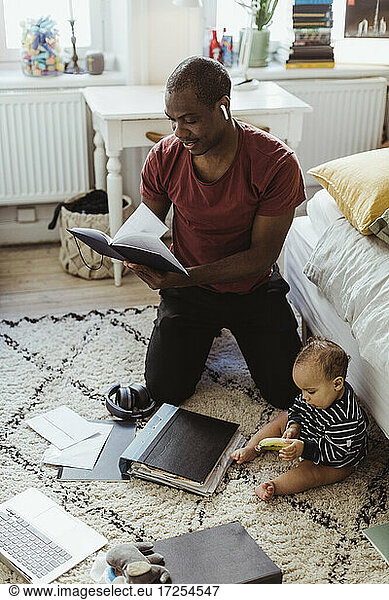 Male entrepreneur kneeling while reading diary by son at home