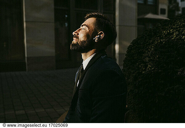 Male entrepreneur listening music through wireless earphones on footpath