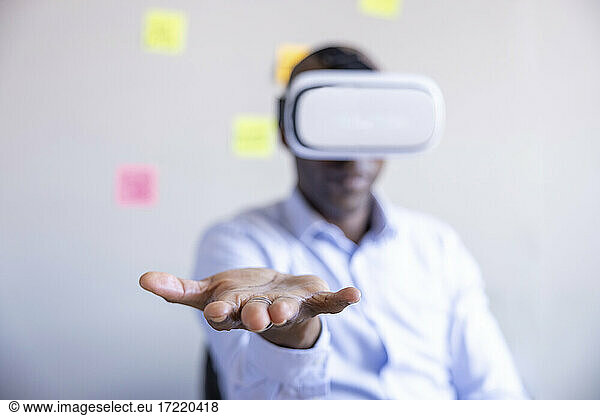 Male entrepreneur showing hand while wearing Virtual reality headset in office