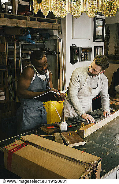Male entrepreneur taking order through phone while colleague working at upcycling workshop