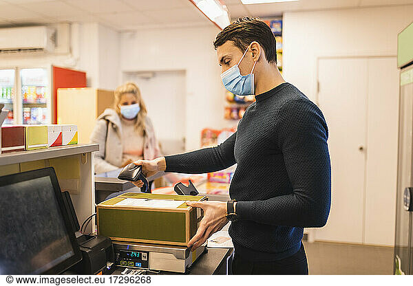 Male entrepreneur using bar code reader on package while female customer standing at checkout during pandemic