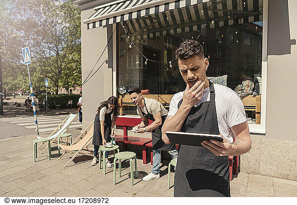 Male entrepreneur using digital tablet while colleagues working in background outside coffee shop