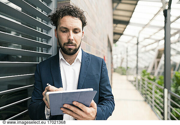 Male entrepreneur using digital tablet while standing in corridor of office