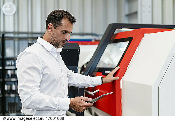 Male entrepreneur using digital tablet while standing in front of machinery at factory