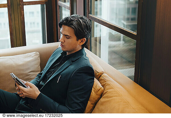 Male entrepreneur using smart phone while sitting on sofa at office