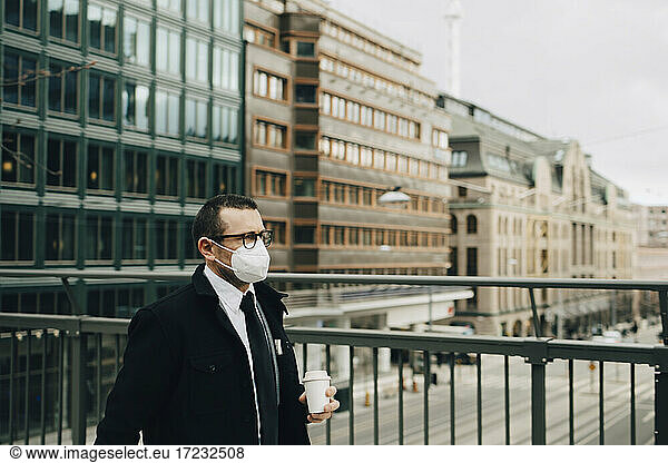 Male entrepreneur with coffee cup by railing in city during pandemic