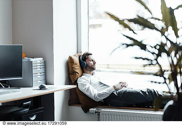 Male entrepreneur with headphones and digital tablet lying by window