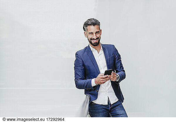 Male entrepreneur with smart phone standing in front of white wall