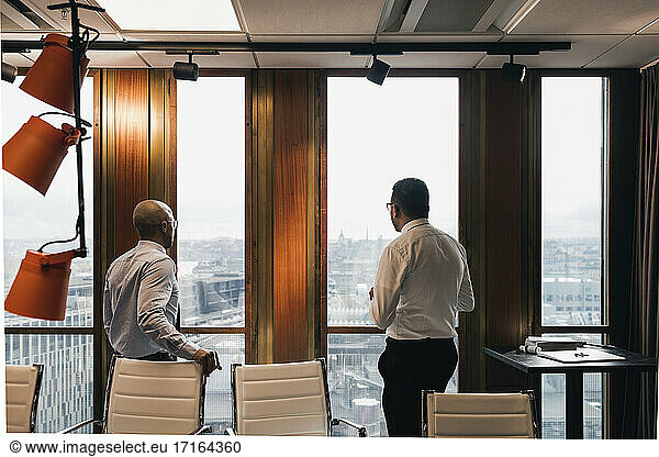 Male entrepreneurs looking through window while planning strategy in board room during meeting