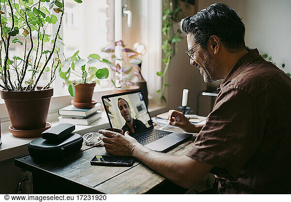 Male entrepreneurs smiling while discussing on video call through laptop at home office