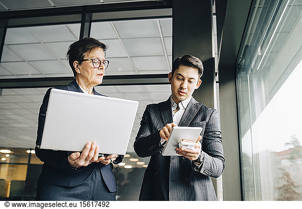 Male executive showing digital tablet to senior professional while standing in office