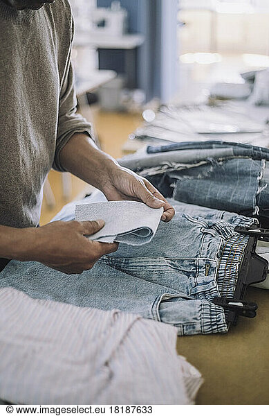 Male fashion designer folding fabric with jeans on workbench at workshop