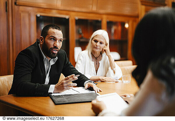 Male financial advisor discussing over contract document with female colleagues in board room