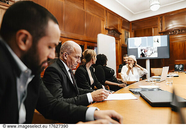 Male financial advisor signing agreement during meeting with colleagues in board room