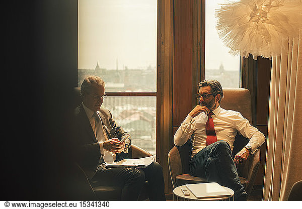 Male financial advisors discussing while sitting against window at law office