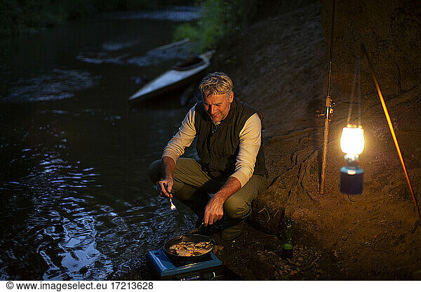 Male fisherman cooking fresh caught fish on camping stove at night