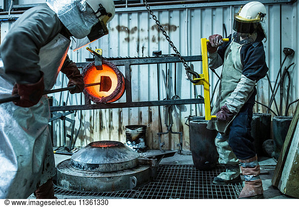 Male foundry worker working with bronze melting pot in bronze foundry