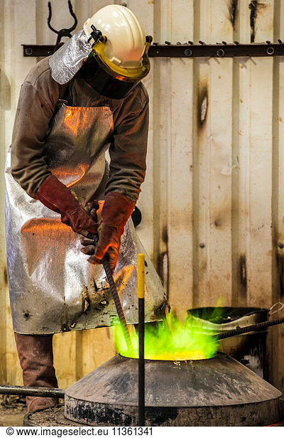 Male foundry worker working with green flamed furnace in bronze foundry