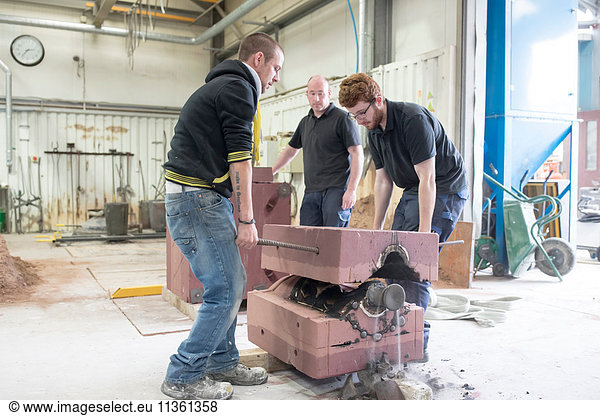 Male foundry workers lifting mould from bronze sculpture in bronze foundry