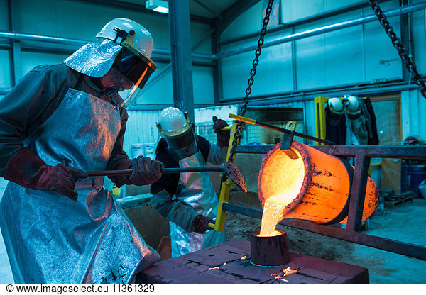 Male foundry workers pouring bronze melting pot in bronze foundry