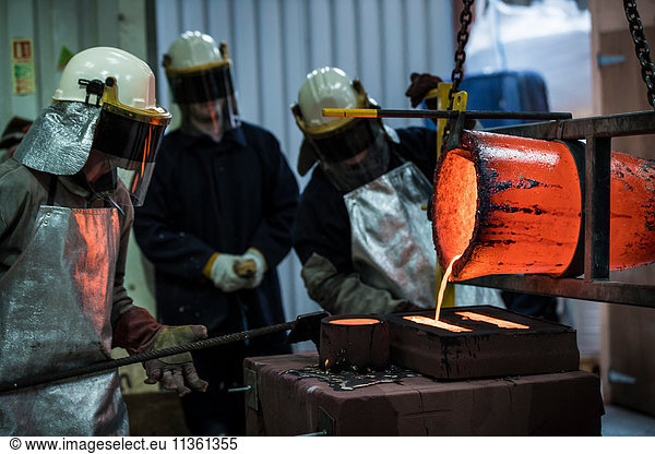 Male foundry workers pouring bronze melting pot in bronze foundry