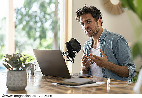 Male freelance worker looking away while podcasting at home office