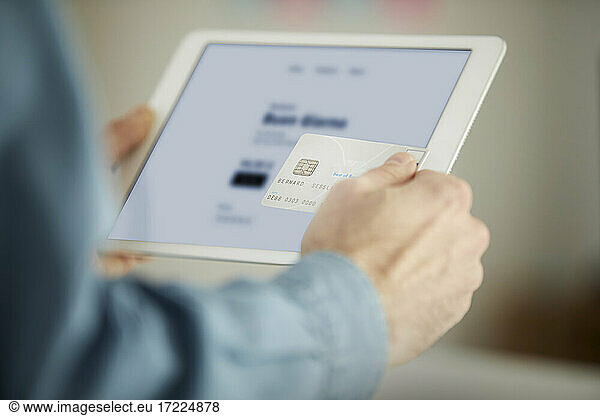 Male freelancer paying through credit card while using digital tablet in office